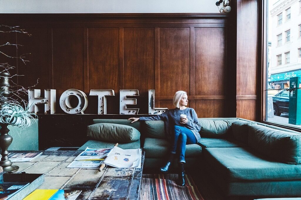A woman sitting on a sofa with a hotel sign behind her. Traveling cheap in hotels.