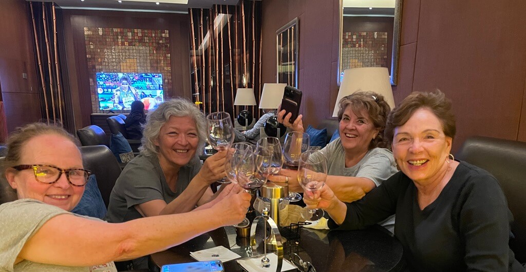 Four women over 50 laughing and clinking glasses